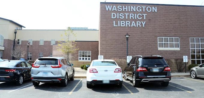 Exterior view of the Washington District Library building with three parked cars in front, photographed on a sunny day.