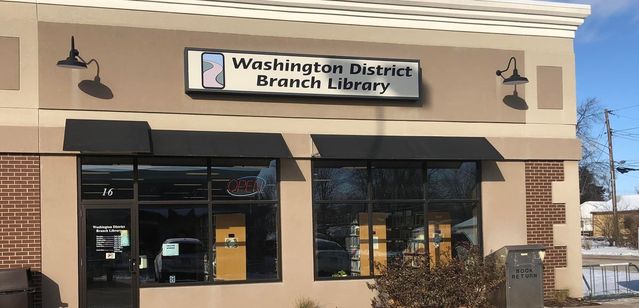 Exterior view of the Washington District Library Sunnyland Branch building with large front windows, black awnings, and landscaped shrubs on a sunny day.